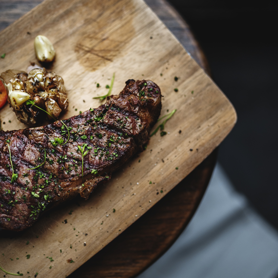 Corte de carne a la parrilla sobre una tabla, con ajo asado y hierbas