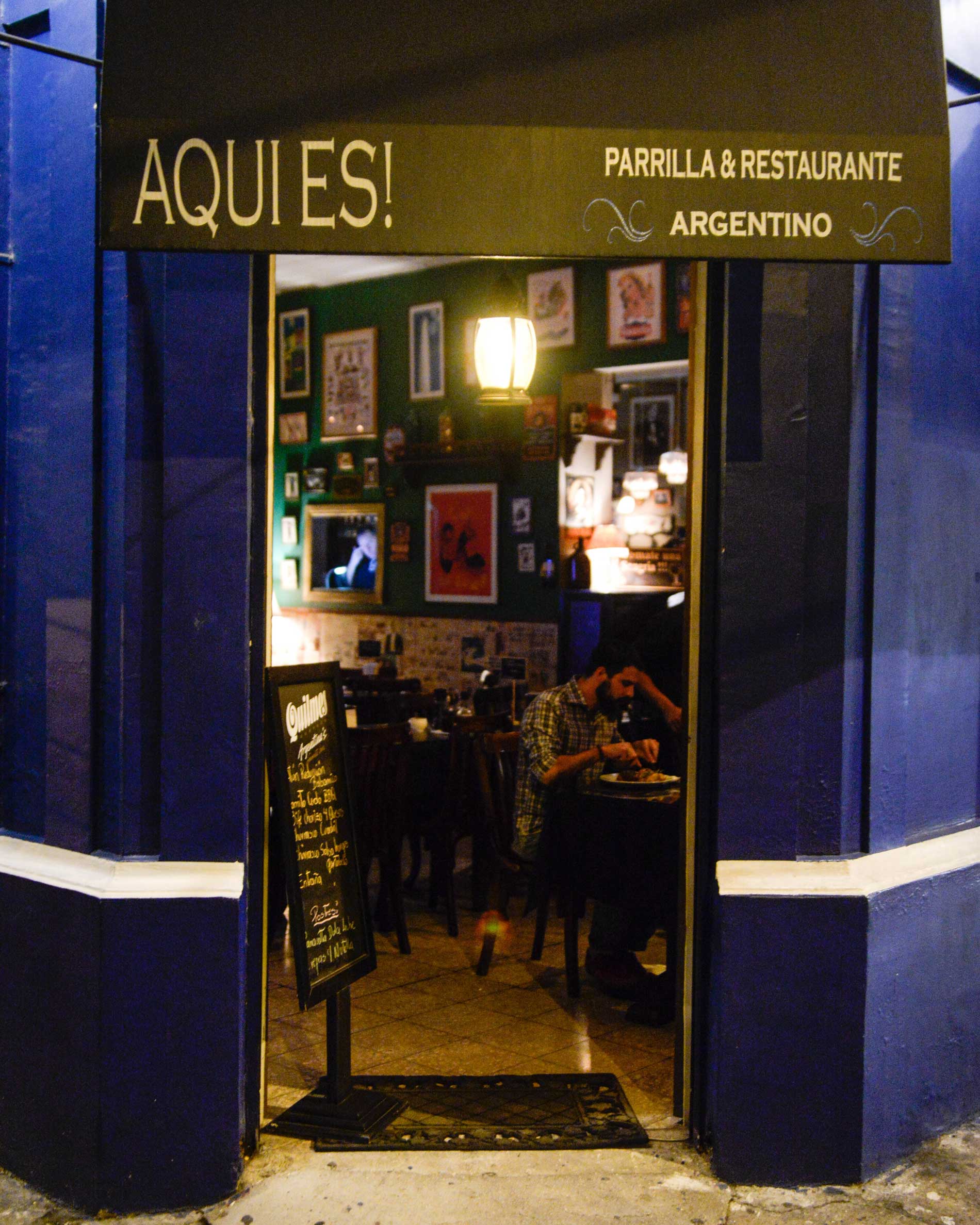 Entrada de Aquí Es, con su fachada azul y letrero del restaurante