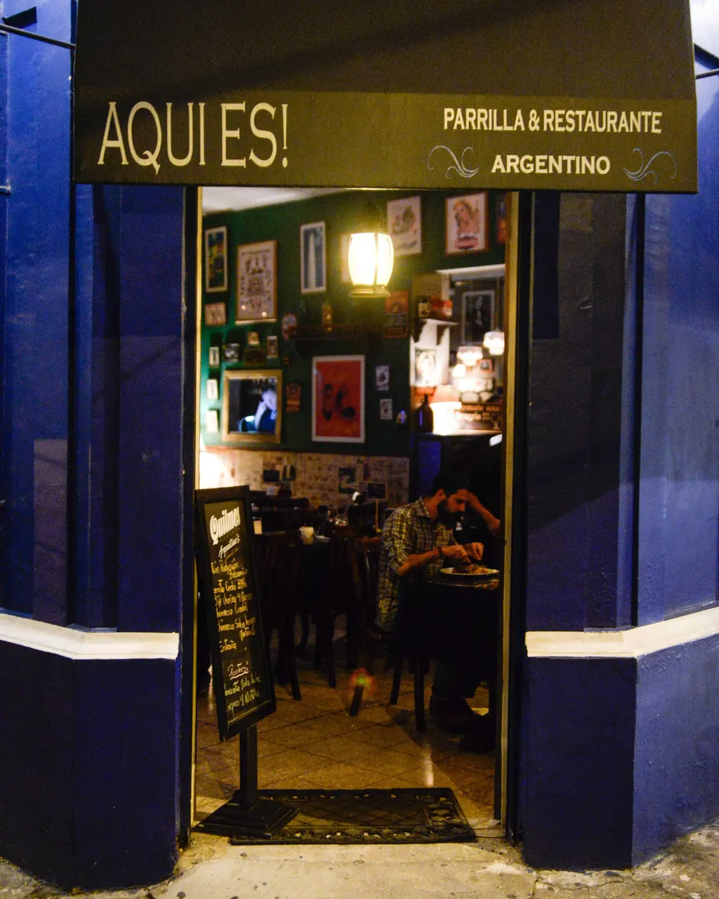 Entrada del restaurante con fachada azul y letrero de Aquí Es