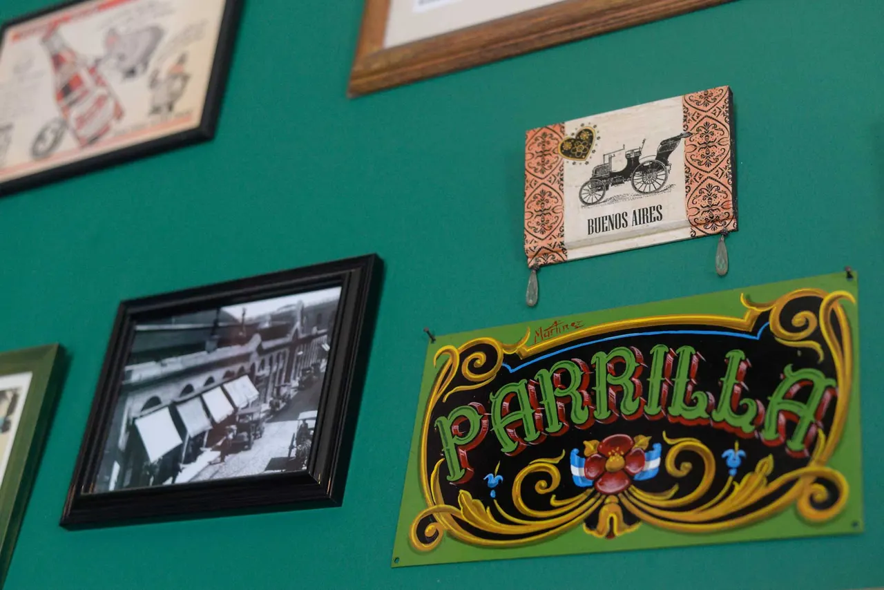 Cartel de parrilla y fotografías argentinas en una pared verde
