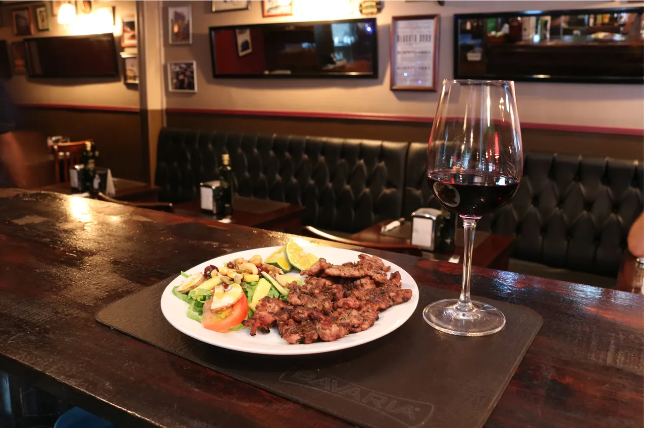 Corte de carne y ensalada junto a una copa de vino